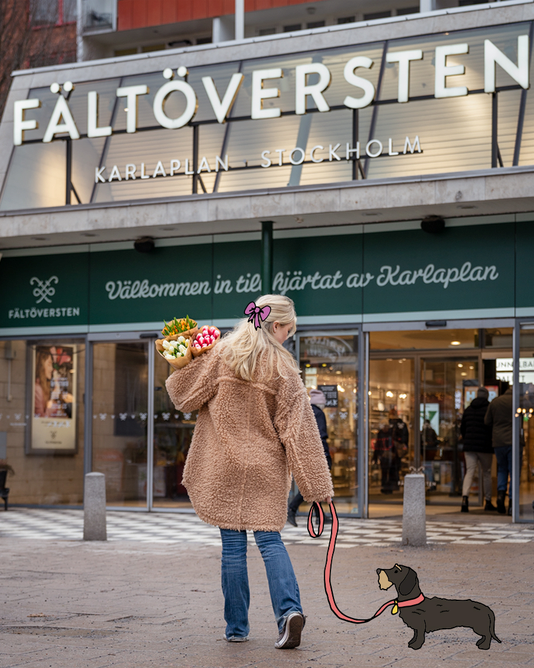 Kvinna med hund och blombukett i handen framför Fältöverstens entré